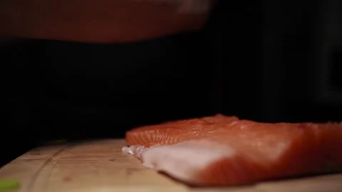 Close-Up of Hands Slicing Fresh Salmon Fillet on a Dark Background Video stock 303926099