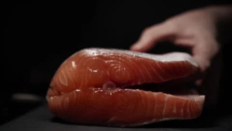 Close-Up of Hands Slicing Fresh Salmon Fillet on a Dark Background Video stock 303926157
