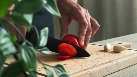 Close-up of hands slicing a fresh tomato on a wooden cutting board Stockbeeldmateriaal 310273682