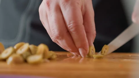Close-up hands slicing green olives on wooden cutting board with chef knife Stock Footage 343677270