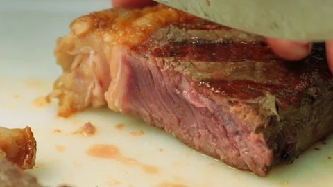 Close up of hands slicing perfectly cooked rare steaks with a knife on a cutt Stock Footage 127715476