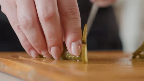 Close-up hands slicing pickled green pepper on wooden cutting board with precise Stock Footage 343675959