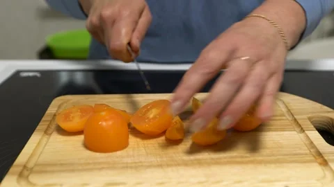 Close-up of hands slicing yellow tomatoes on a wooden cutting board with a knife Stock Footage 336444209