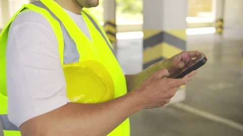 Close up hands with smartphone, an engineer in a safety vest holds a helmet and Stock Footage 348244867