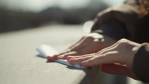 Close up hands smoothing folded paper on concrete in soft sunlight with outdoor 库存影片 348114953
