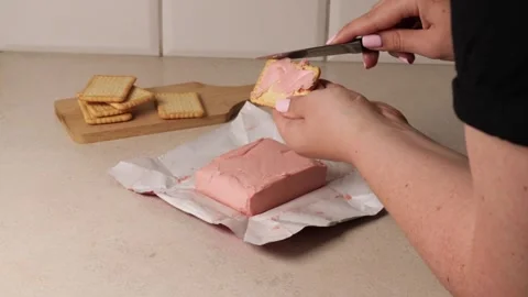 Close-up of hands spreading creamy pink raspberry butter onto a biscuit using a Stock Footage 314011990