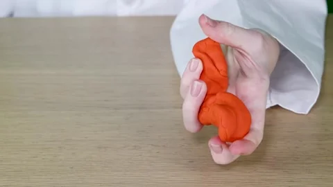 Close Up of Hands Squeezing Orange Modeling Clay on Wooden Table Stock Footage 325828171