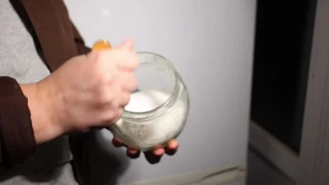 Close-up of hands stirring white granular substance in a glass jar with a spoon Stock Footage 339179470