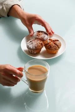 Close up of hands taking one of three curd muffin, and holding glass cup of.. Stock Photos