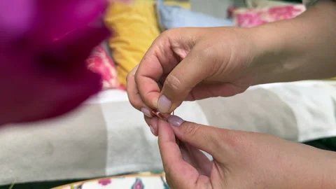 Close-up of hands threading a needle with bright colored thread. The image captu Stock Footage 311476814