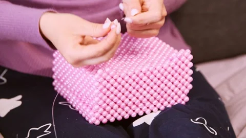 Close up hands threading pink beads forming square beadwork box on lap with.. Stock Footage 334570431