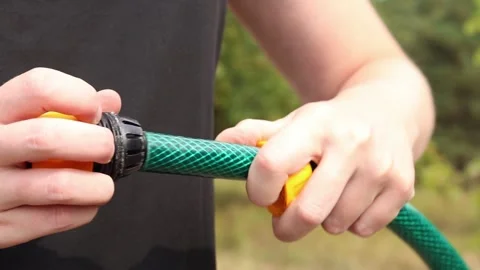 Close-up of hands tightening yellow plastic connector on green garden hose Stockbeeldmateriaal 344879106