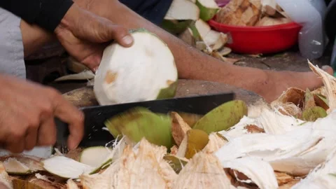 Close-up of hands trimming a fresh coconut, exposing its white surface under Stock Footage 313486111