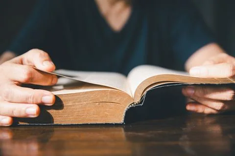Close-up of hands turning pages of an old Bible on a wooden table, represen.. Stock Photos