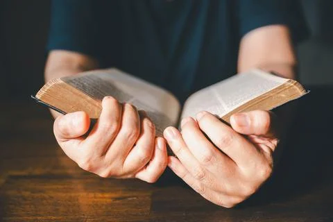 Close-up of hands turning pages of an old Bible on a wooden table, represen.. Stock Photos
