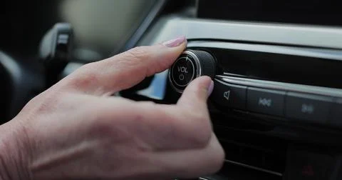 Close-up of hands turning volume button of car radio. Woman driving car. Li.. Stock Photos