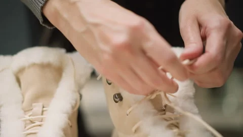 Close up of hands tying laces on beige fur lined boots with visible texture Stock Footage 346731152