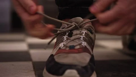 Close-up of hands tying the laces on a worn sneaker, indoor lighting Video stock 270078675