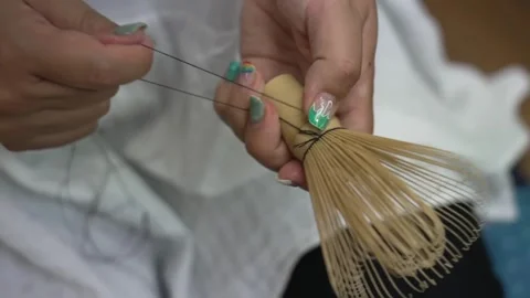 Close up of hands tying thread around the bamboo tines of a handmade matcha Stock Footage 348236975
