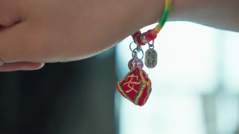 Close-up of Hands Tying Traditional Red Green Bracelet with Charms Stock Footage 339069060