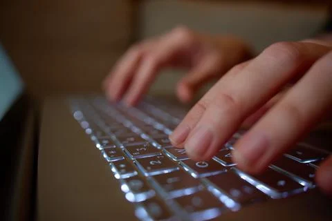 Close up of hands typing on backlit laptop keyboard in dim light. Concept of Stock Photos
