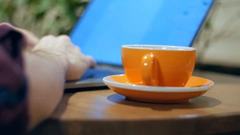 Close-up of hands typing on a laptop and an orange coffee cup, drinking from it Vídeo Stock 101710954