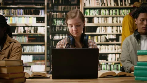 Close-up of hands typing on laptop beside open book on library table Stock Footage 337229884