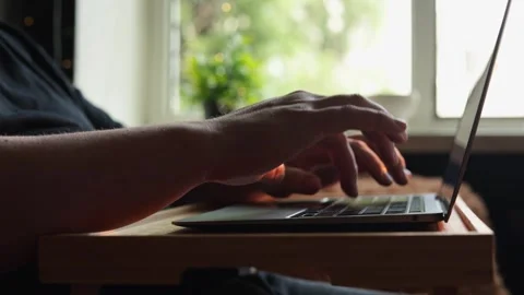 Close-up of hands typing on a laptop with a blurred window view in the Stock Footage 340264387