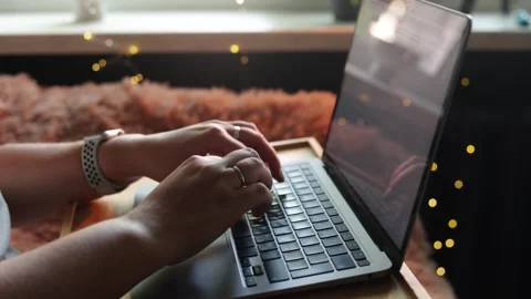 Close-up of hands typing on a laptop with cozy fairy lights in the background Stock Footage 340265260
