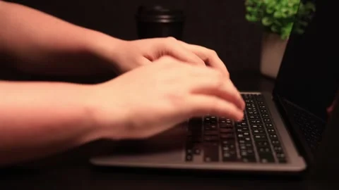 Close-up of hands typing on a laptop keyboard with a coffee cup and plant in the Stock Footage 338432506