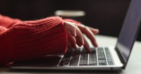 Close-up of hands typing on a laptop keyboard wearing a cozy red sweater Stock Footage 339073562