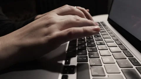 Close-up of hands typing on a laptop keyboard in low light, focusing on the Stock Footage 339174399