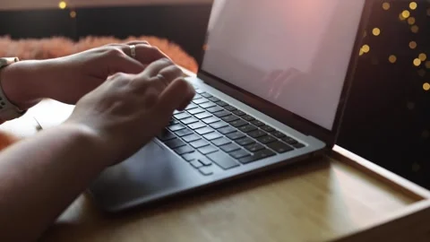 Close-up of hands typing on a laptop keyboard with warm bokeh lights in Stock Footage 340265224
