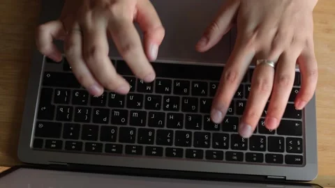 Close-up of hands typing on a laptop keyboard with a wooden desk background Stock Footage 340265317