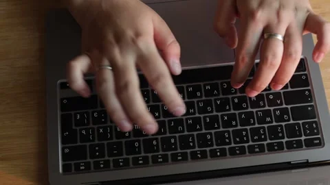 Close-up of hands typing on a laptop keyboard with a wooden desk background Stock Footage 340265372
