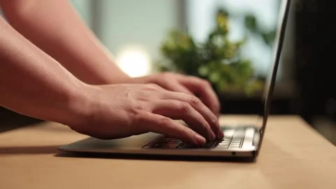 Close-up of hands typing on a laptop keyboard with a plant in the background Vidéo 341737632