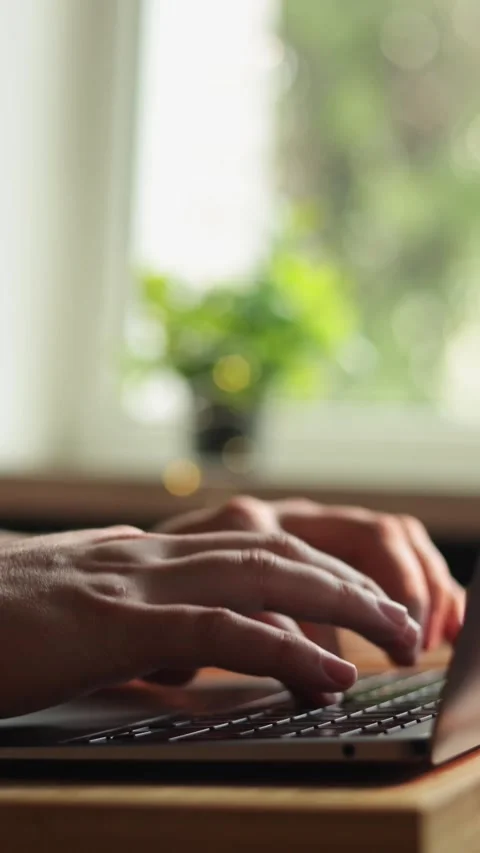 Close-up of hands typing on a laptop keyboard with a blurred green background Vidéo 343838126