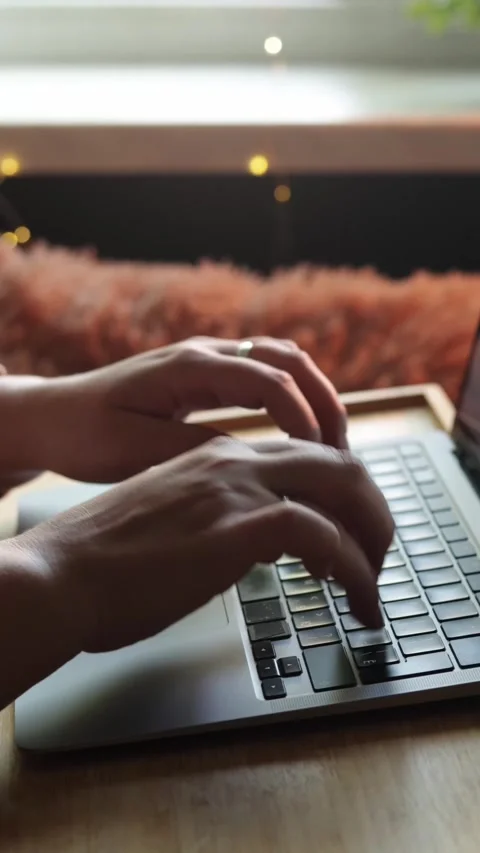 Close-up of hands typing on a laptop keyboard with warm ambient lighting Vidéo 343838168