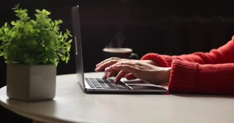 Close-up of hands typing on a laptop next to a potted plant and steaming coffee Stock Footage 339072572