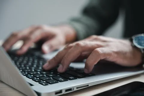 Close up of hands typing on a silver laptop keyboard. The background is out.. Stock Photos