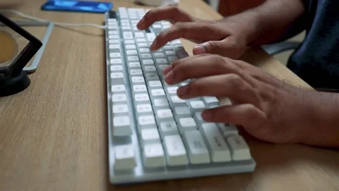 Close-up of hands typing on a white mechanical keyboard on a wooden desk Stock Footage 315981465