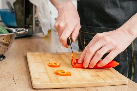 Close up of hands of unrecognizable man chop red bell pepper with knife on Stock Photos