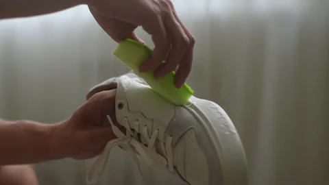Close-up hands of unrecognizable man washing dirty white shoes using sponge and Stock Footage 263869020