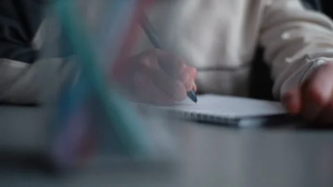 Close-up hands of unrecognizable pupil boy writing notes in workbook sitting at Stock Footage 151027080