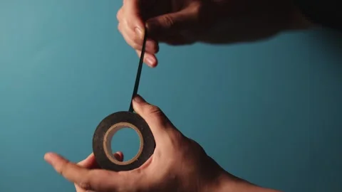 Close-up of hands unrolling black electrical tape against a blue background Stock Footage 340268473