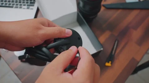 Close-up of hands unwrapping a black electronic device with a cable on a wooden Stock Footage 333321421