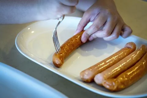 Close-up hands use fork puncturing homemade sausage. Stock Photos