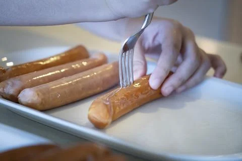 Close-up hands use fork puncturing homemade sausage. Stock Photos