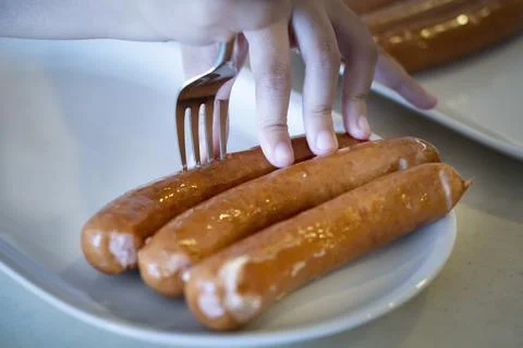 Close-up hands use fork puncturing homemade sausage. Stock Photos