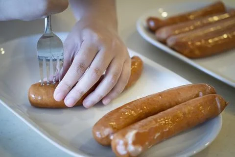 Close-up hands use fork puncturing homemade sausage. Stock Photos